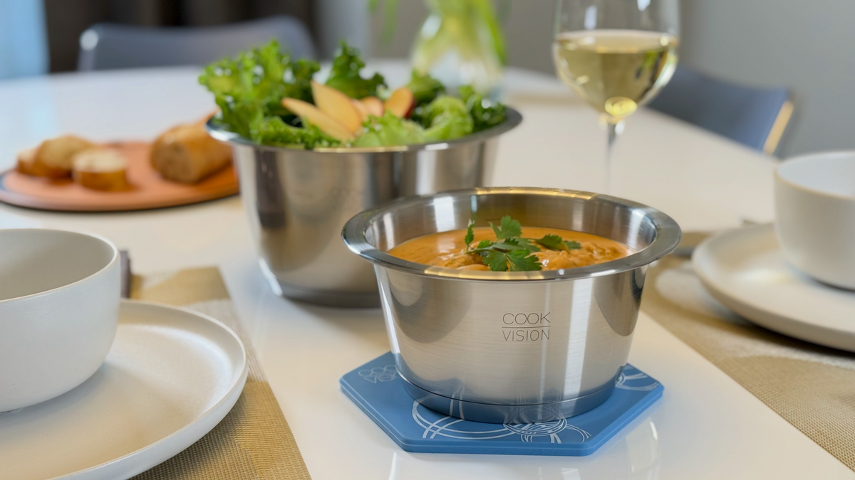 nesto Stainless steel pots with food on a dining table with a glass of wine and salad.